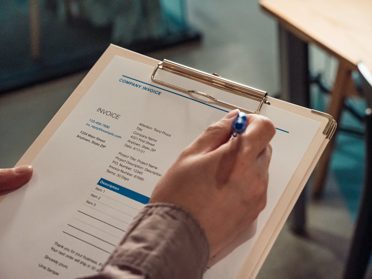 Persons hand holding a company invoice on a clipboard with a pen.